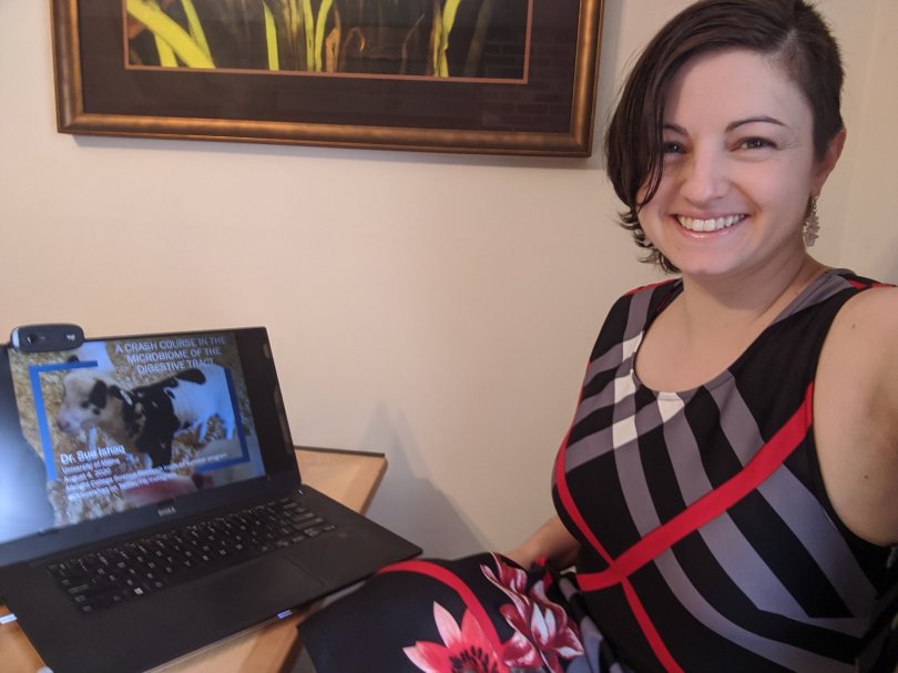 Woman in a dress sitting in front of a laptop displaying the title slide to a presentation called "Microbes on the Farm".