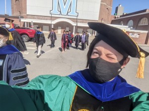 Sue talking a selfie in the UMaine parking lot in full regalia.