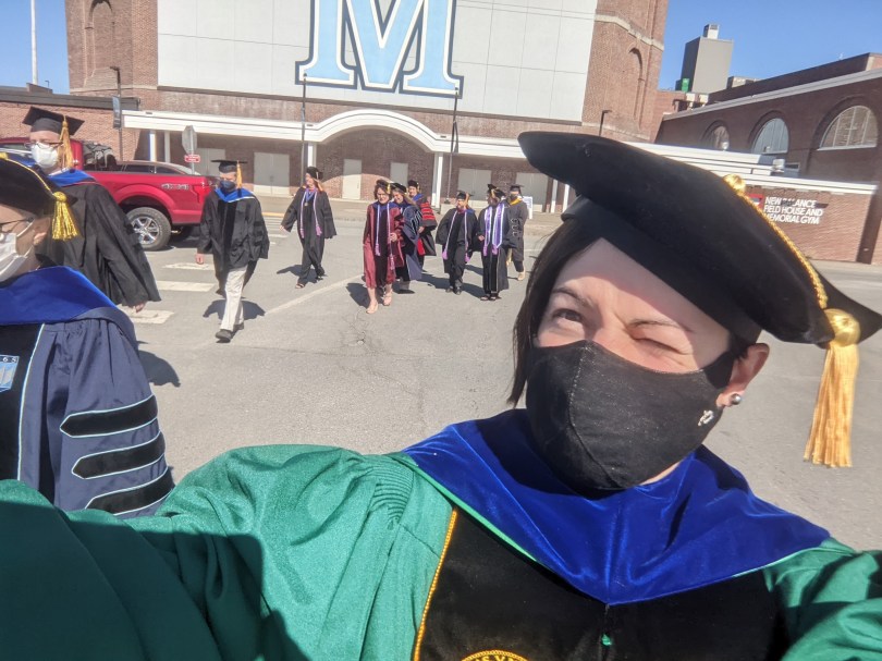 Sue talking a selfie in the UMaine parking lot in full regalia.