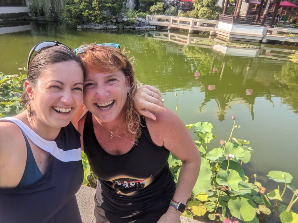 Two women laughing and posing for a photo in front of a koy pond.