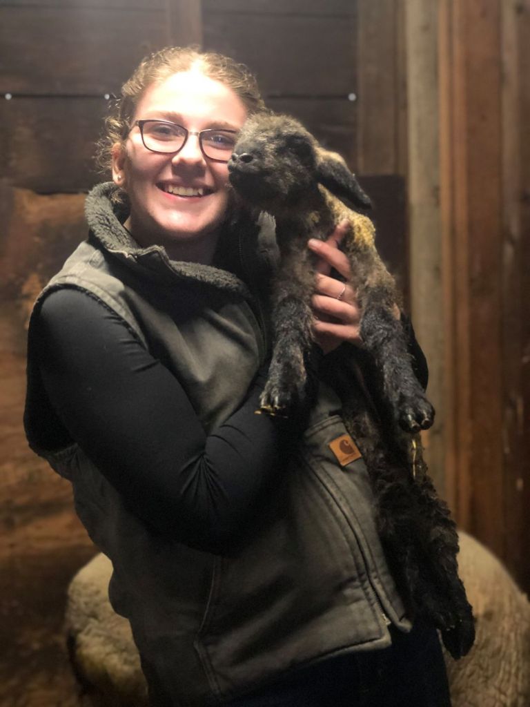 Emily Sala holding up a newborn lamb.