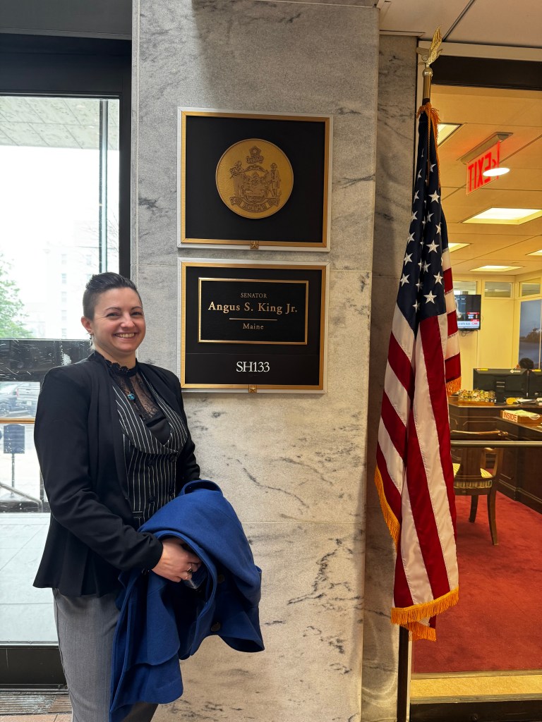 A person in a suit standing outside the DC office for Senator Angus King.
